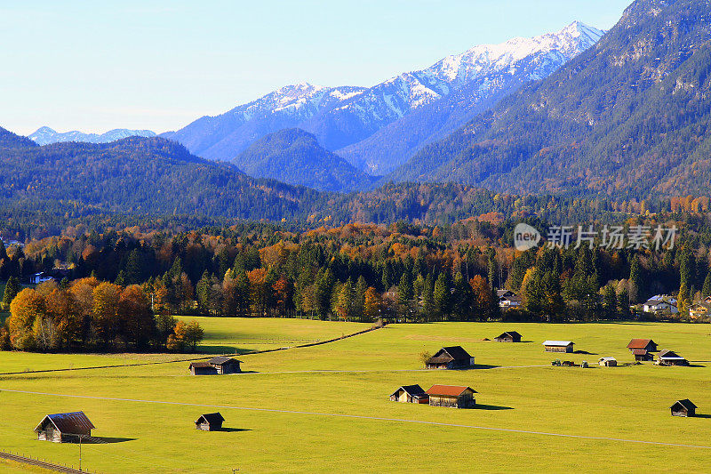 在谷仓农场和小木屋之上，阳光明媚的Garmisch Partenkirchen阿尔卑斯村庄在巴伐利亚阿尔卑斯山从Alpspitze，田园诗般的松树林地秋季景观，雄伟的阿尔卑斯山谷，戏剧性的巴伐利亚德国雪山全景，德国